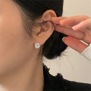 Close-up of minimalist silver stud earrings with iridescent shell inlay on model's ear