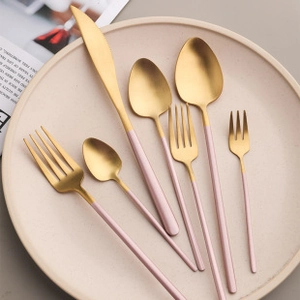 Künstlerisches Besteckset in Gold und Rosa auf einem beigen Keramikteller serviert