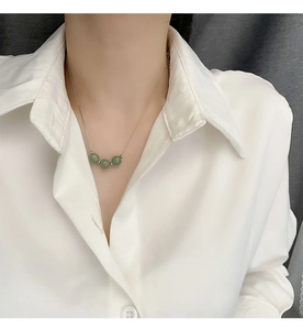 Detail of jade bead pendant necklace in stainless steel on a white shirt