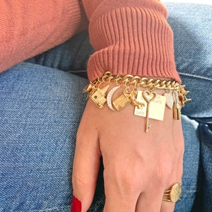 Gold stainless steel link bracelet with house and heart charms worn on a casual background