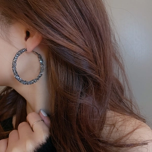 Close-up of oversized dark grey geometric hoop earrings with shimmering crystals on model