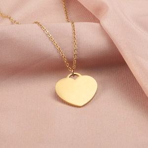 Close-up of golden heart pendant on a thin link chain over pink silk fabric