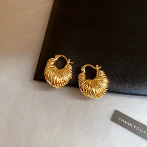 Close-up of gold-plated U-shaped earrings with intricate woven texture on dark leather