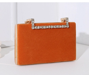 Seitliches Detail einer orangefarbenen Samt-Abendtasche mit glitzerndem Strassgriff.