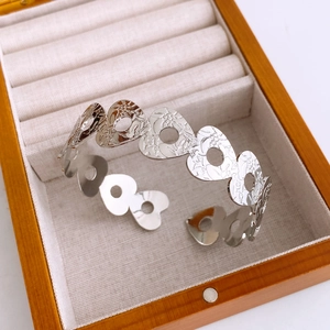 Detail of silver open bangle featuring hollow heart patterns and embossed textures