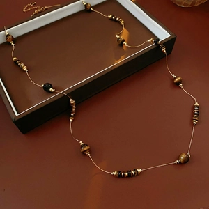 Détail d'un collier vintage avec perles oeil de tigre marron et chaîne métal sur fond rétro