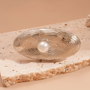 Close-up of silver oval textured hair clip with a centered white pearl on stone