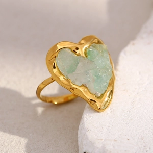Detail of 18K gold heart ring with green tiger eye crushed stones on white rock