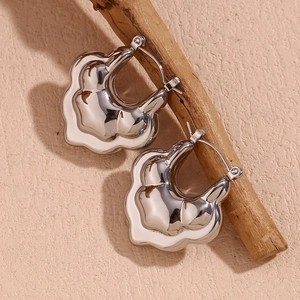 Macro detail of silver wavy hollow lotus hoop earrings on a natural wood branch