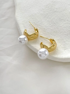 Gros plan de boucles d'oreilles dorées avec perles blanches au design irrégulier