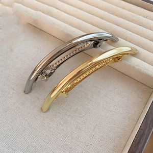Close-up of minimalist curved metal hair clips in polished gold and silver finishes