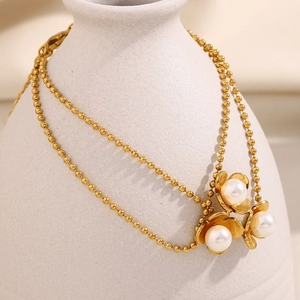 Close-up of 18K gold beaded chain with three floral pendants and pearls on a vase