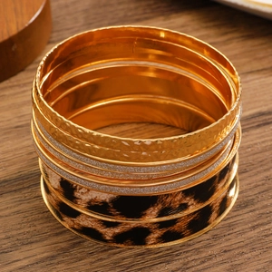 Macro shot of vintage leopard print and textured gold multi-layered bangle set on wood