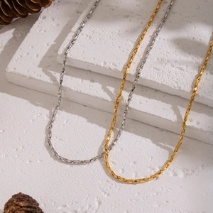 Minimalist geometric link chains in gold and silver finish on stone pedestal