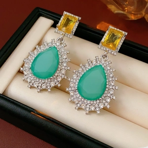 Détail de boucles d'oreilles vintage avec pierres vertes et jaunes dans un écrin