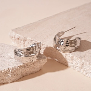 Detailed view of silver C-shaped earrings with irregular crushed metal texture on stone