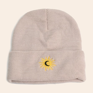 Close-up of the sun and moon embroidery on a beige thick knitted beanie hat