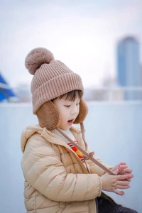 Close-up of warm khaki knit baby winter hat with large pom-pom and ear flaps