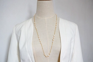 Detail of a long layered gold chain necklace with freshwater pearls on a white blazer mannequin