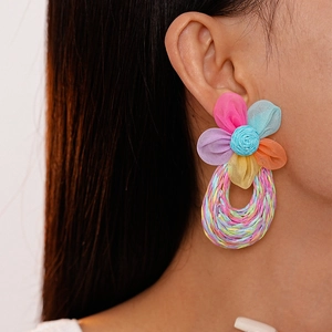Detail of colorful hand-woven lace flower and raffia hoop earrings on model ear