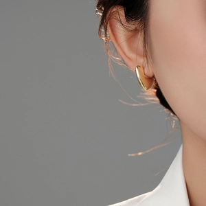 Close-up of a minimalist gold heart earring worn by a model against a grey background