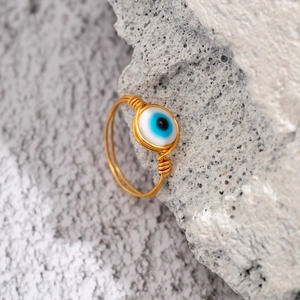 Macro shot of handmade gold wire-wrapped ring featuring a blue opal evil eye bead detail