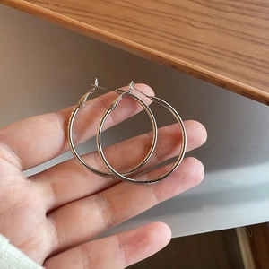 Detail view of round silver hoop earrings held by hand showing the polished metallic finish