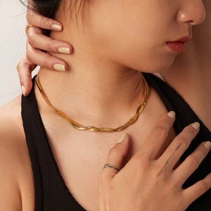 Detail of a two-tone twisted snake chain necklace and a gold ring on a model