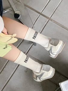 Detail of cream cotton crew socks with PASSION text paired with silver sneakers