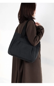 Side view of large black canvas tote bag on female model with minimalist shoulder design
