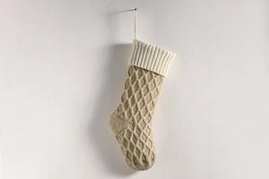 Nahaufnahme beiger Strick-Weihnachtsstrumpf mit weißem Rippbündchen an einer weißen Wand