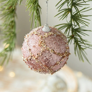 Sparkly pink sequined Christmas ball ornament with glitter hanging on a festive green pine branch