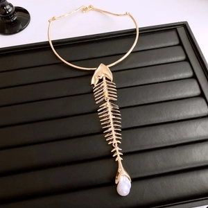 Detailed view of a gold fishbone pendant necklace with a white baroque pearl on black tray