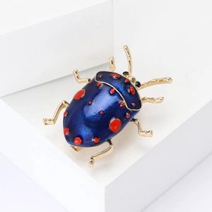 Creative beetle brooch with deep blue enamel and red spots on a white pedestal