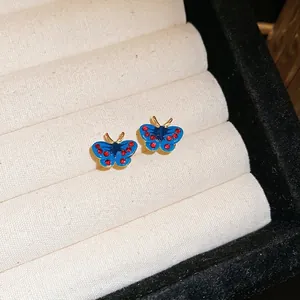 Elegant butterfly stud earrings with blue enamel and red rhinestones on white velvet base