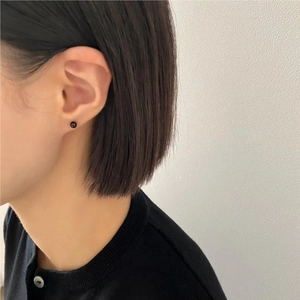 Close-up of a minimalist small black round stud earring worn on a model ear lobe
