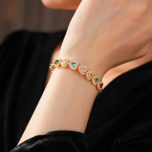 Close-up of a model wearing a gold bracelet with colorful heart-shaped zircons