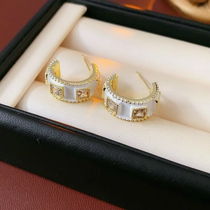 Close-up of C-shaped earrings with white enamel and square cubic zirconia stones