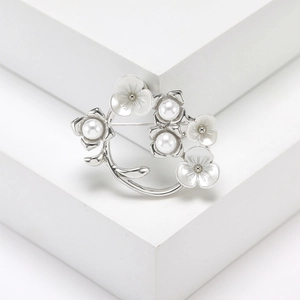 Elegant silver flower vine brooch with white enamel petals and pearls on a white stand