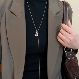 Close-up of a silver necklace with a brown tiger eye heart pendant on a dark sweater