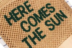 Détail du lettrage brodé 'HERE COMES THE SUN' sur un grand sac cabas en paille tissé