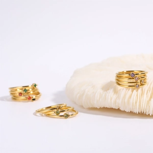 Detail view of stacked gold birthstone rings with colorful gems on a white coral base