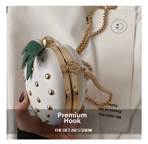 Detail shot of strawberry-shaped bag with gold rivets, green leaf accents, and chain