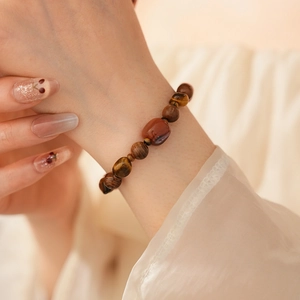 Détail d'un bracelet en perles d'œil de tigre, agate rouge et bois sur fond de tissu
