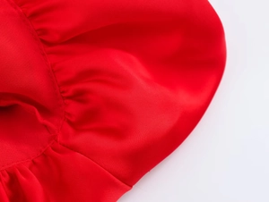 Détail macro du tissu satin rouge montrant un éclat de soie et des volants plissés