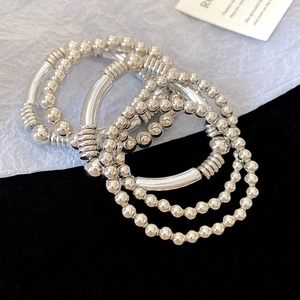 Close-up of silver beaded bracelets with metallic tubes on black and white texture