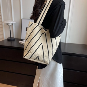 Beige knitted tote bag with black geometric stripes worn by a model for a daily commute