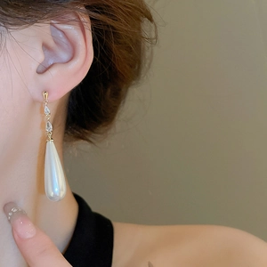Macro view of long gold drop pearl earrings with rhinestone accents on elegant model