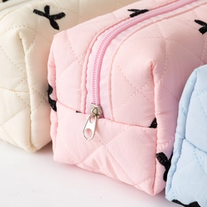 Quilted fabric cosmetic pouches with black bow embroidery in beige, pink and blue colors