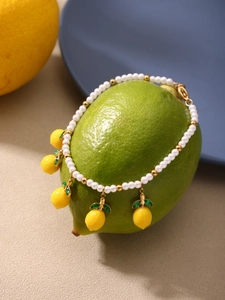 Detail of pearl bracelet with five lemon pendants and gold beads on a fresh lemon